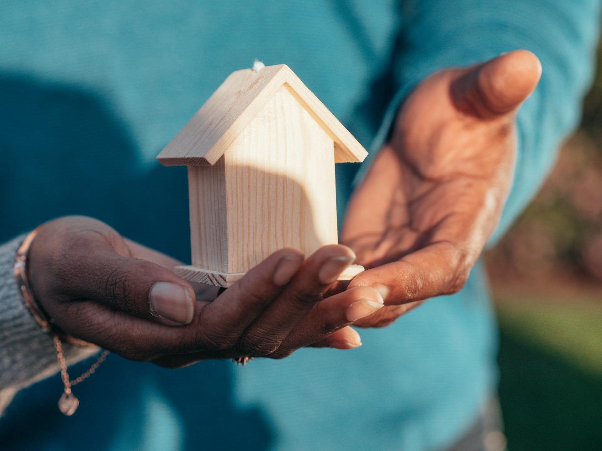 Cupped hands holding a small wooden model house